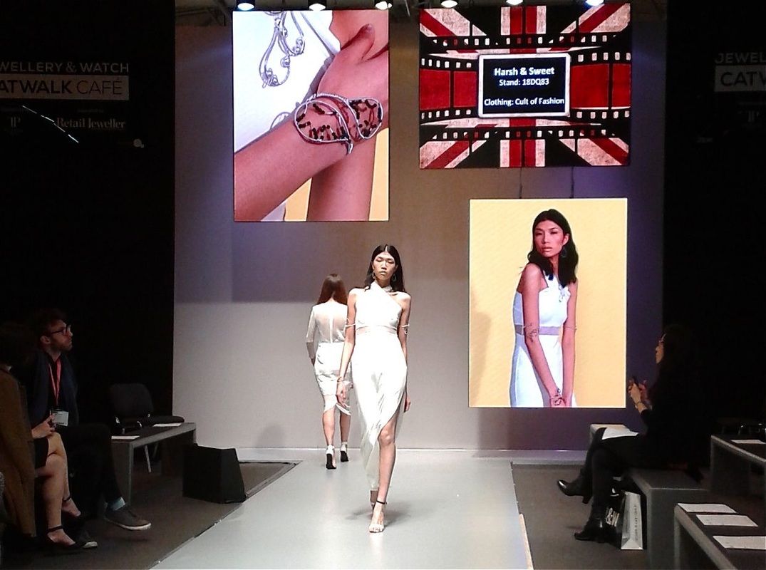 Models on catwalk. Once of them is modeling Harsh and Sweets' jewelry that is also shown on a background display.
